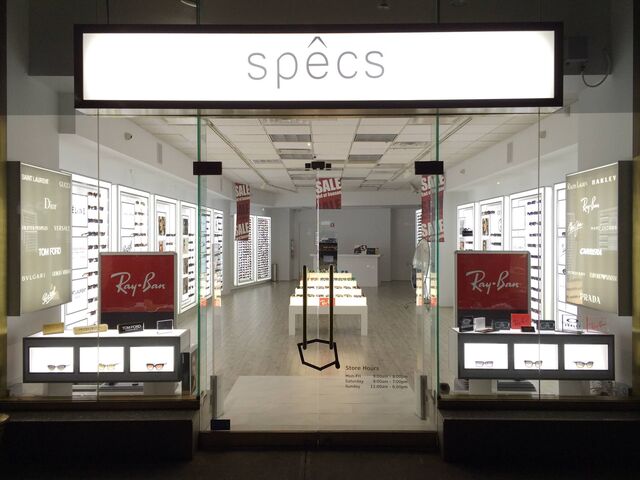 Head-on view of the Specs storefront with logos of Ray Bans, Tom Ford, Dior and more on the walls