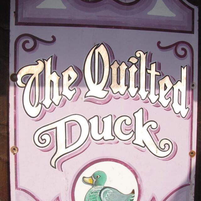 Logotype for The Quilted Duck in large, caligraphy-esque light violet colors